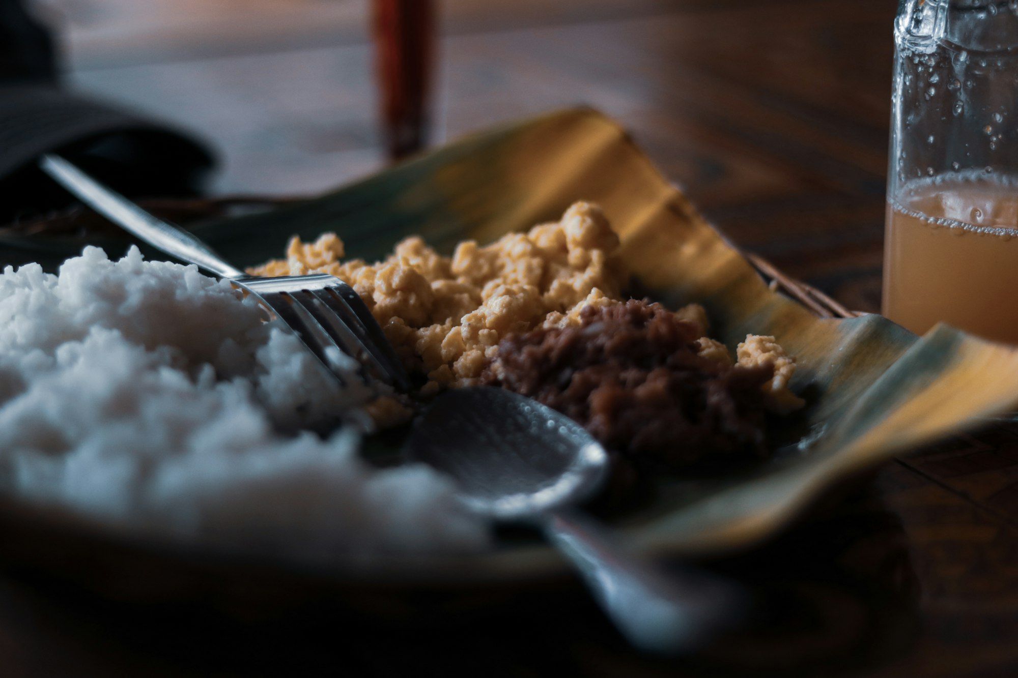 Nasi putih, telur orak-arik berbumbu, dan sambal daging di atas daun pisang, dengan garpu dan sendok logam di sampingnya