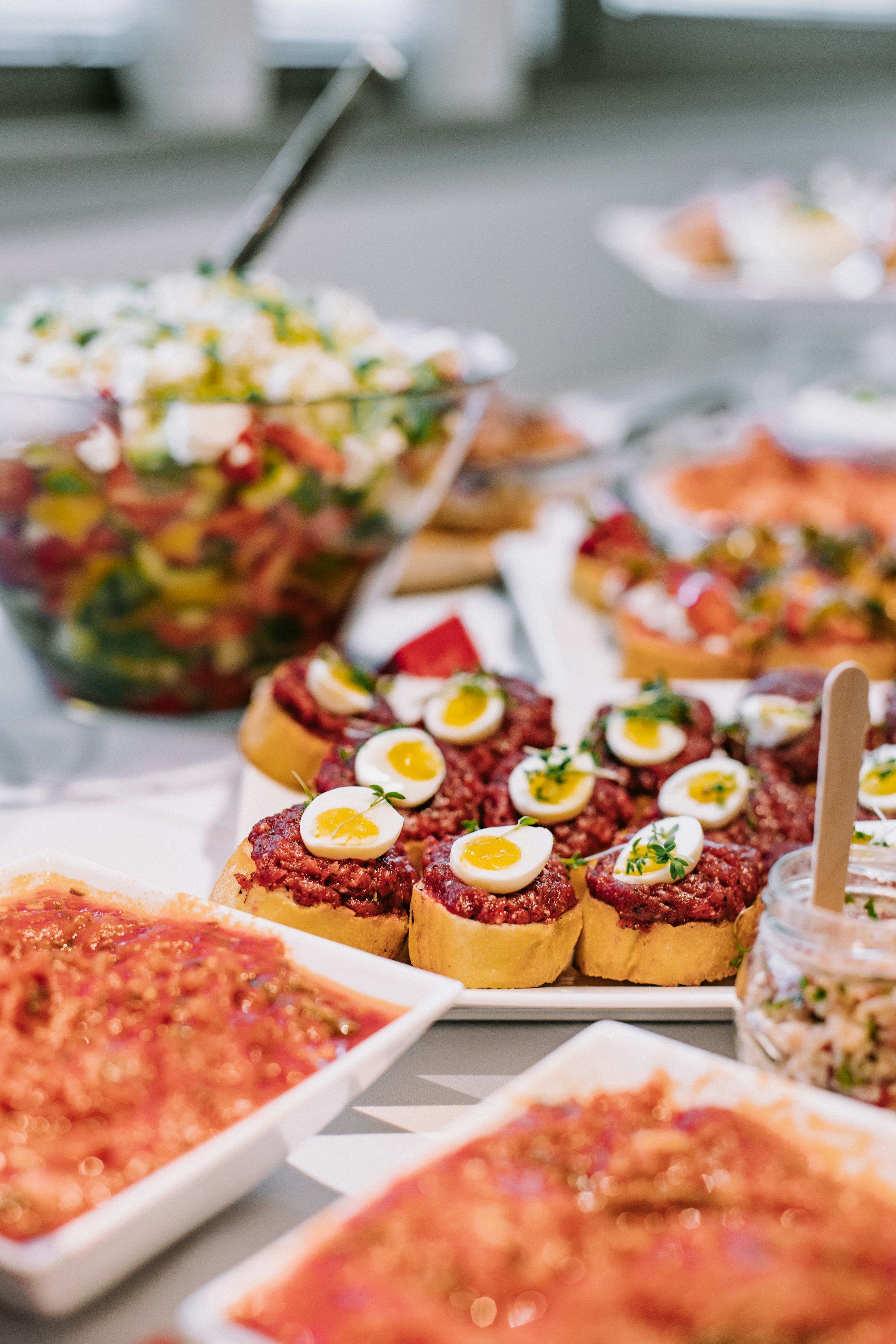 Nampan canape roti panggang bertopping telur puyuh, dikelilingi mangkuk salad dan sambal di meja putih